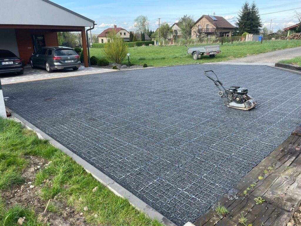 Gravel-filled Ecoraster permeable grid driveway being compacted to fix drainage problems and prevent standing water